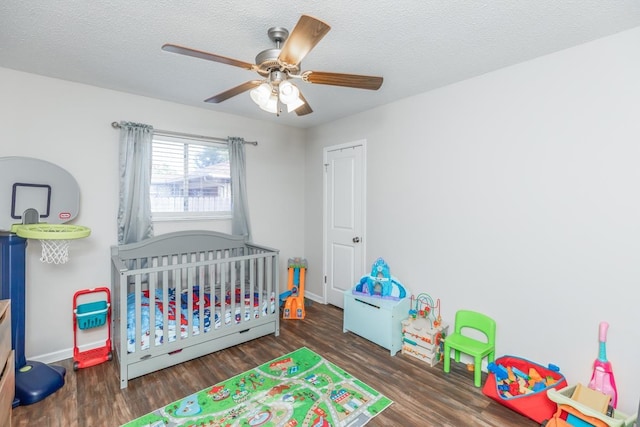 bedroom with ceiling fan, dark hardwood / wood-style flooring, a textured ceiling, and a nursery area