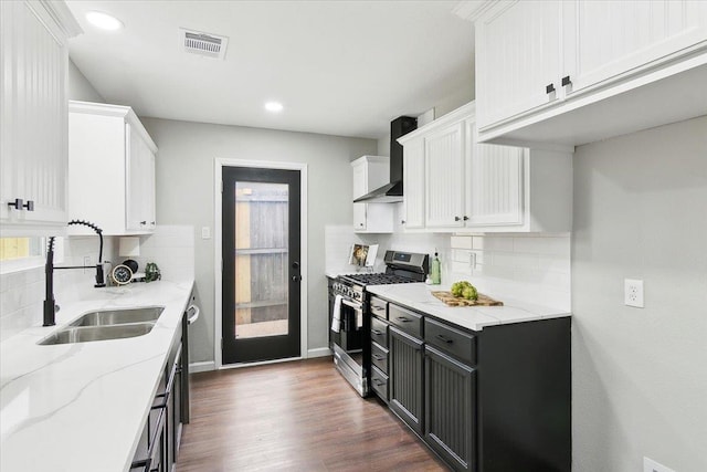 kitchen featuring a sink, visible vents, white cabinets, wall chimney range hood, and stainless steel range with gas cooktop