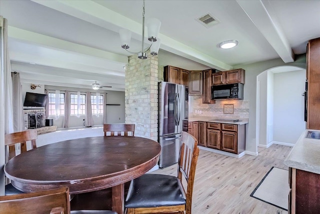 dining space featuring visible vents, beamed ceiling, arched walkways, a fireplace, and ceiling fan