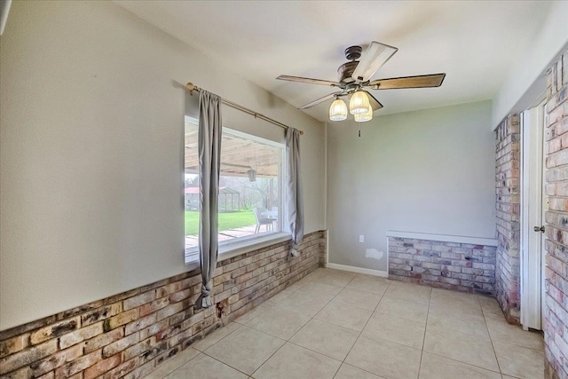 spare room with light tile patterned floors, a ceiling fan, baseboards, and brick wall