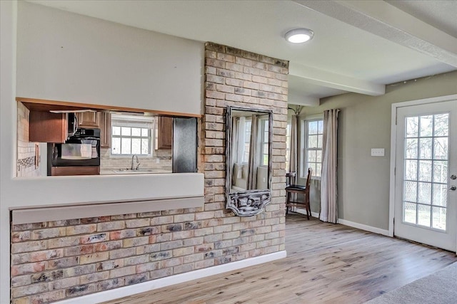 kitchen with oven, beam ceiling, light wood-style flooring, a sink, and baseboards