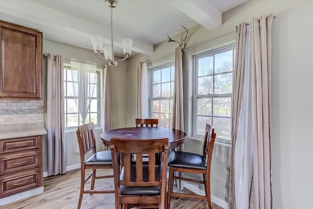 dining area with baseboards, beam ceiling, an inviting chandelier, and light wood finished floors