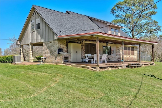 rear view of property featuring a yard, roof with shingles, board and batten siding, a fireplace, and central AC unit