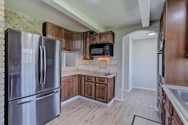 kitchen with black appliances, beamed ceiling, arched walkways, and backsplash