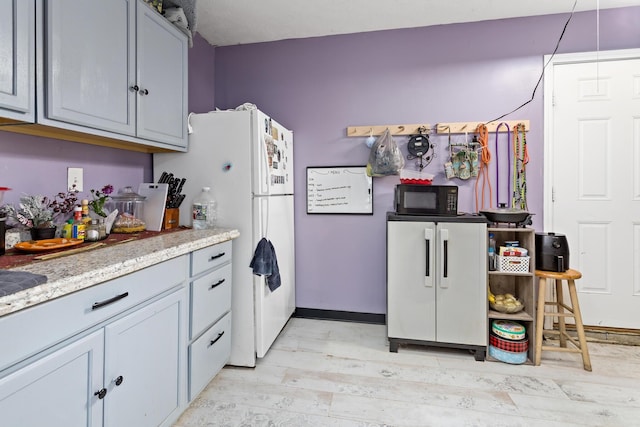 kitchen featuring freestanding refrigerator, black microwave, and light wood finished floors