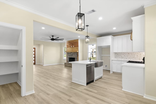 103 Ned, Lumberton, TX 77657 - kitchen with stainless steel dishwasher, hanging light fixtures, a fireplace, white cabinetry, and light wood-style flooring