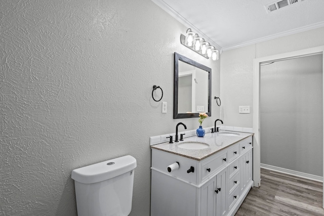 full bathroom featuring ornamental molding, wood finished floors, double vanity, toilet, and a textured wall