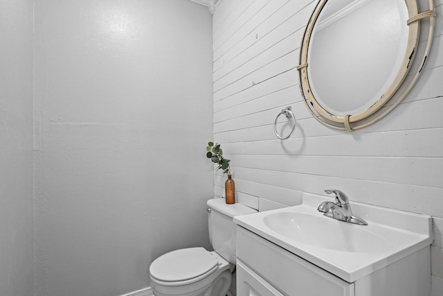 half bath with wooden walls, vanity, and toilet