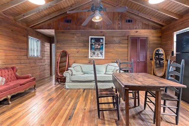 dining area featuring vaulted ceiling with beams, wood walls, wood ceiling, and light hardwood / wood-style flooring