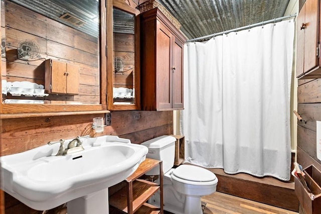 bathroom with hardwood / wood-style floors, toilet, sink, and wooden walls