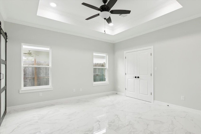 unfurnished room with a tray ceiling, a barn door, ceiling fan, and ornamental molding