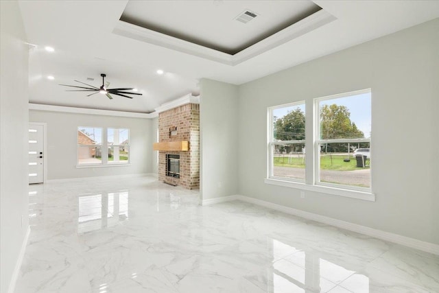 unfurnished living room with ceiling fan, ornamental molding, a fireplace, and a tray ceiling