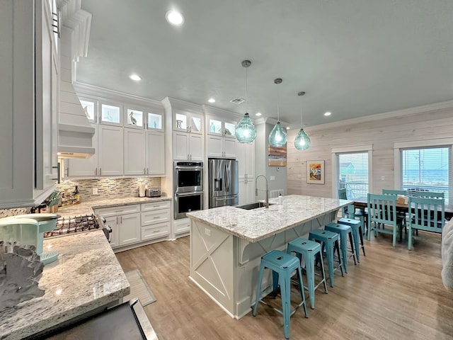 kitchen with crown molding, a center island with sink, stainless steel appliances, and a sink