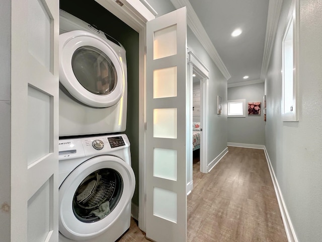 laundry room featuring stacked washer and clothes dryer, crown molding, light wood-style floors, laundry area, and baseboards