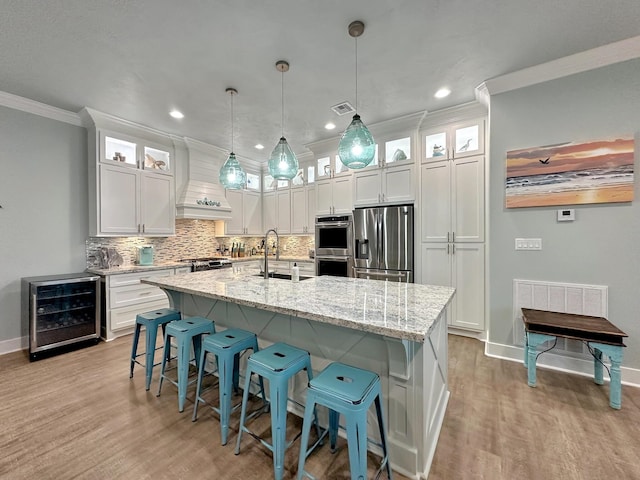 kitchen featuring wine cooler, stainless steel appliances, visible vents, a sink, and premium range hood