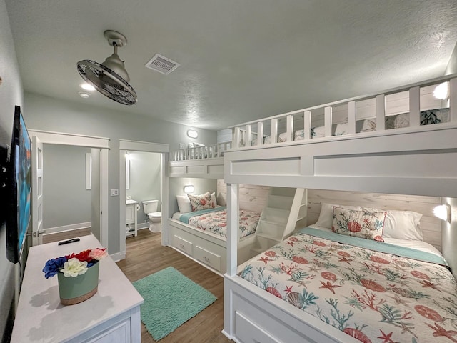 bedroom featuring ensuite bath, visible vents, and wood finished floors