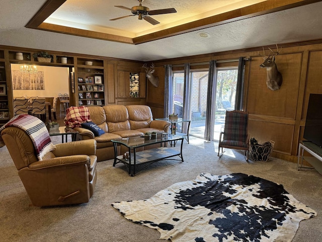 carpeted living area featuring built in features, a raised ceiling, wood walls, ceiling fan, and a textured ceiling