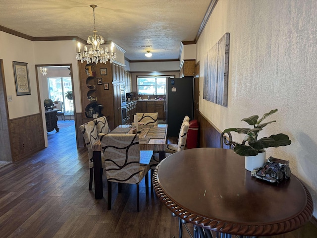 dining area with a textured ceiling, a wainscoted wall, crown molding, dark wood-style floors, and an inviting chandelier