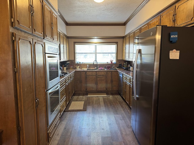 kitchen featuring dark countertops, appliances with stainless steel finishes, ornamental molding, a sink, and a textured ceiling