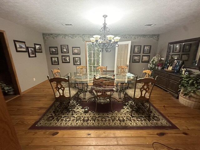 dining room with hardwood / wood-style floors, a textured ceiling, and an inviting chandelier