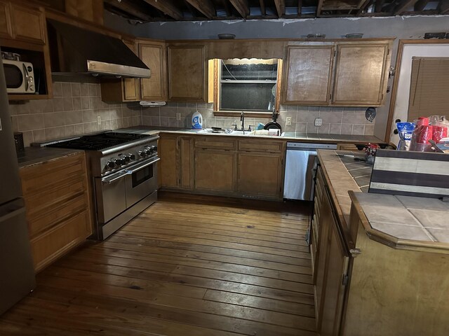 kitchen featuring tasteful backsplash, wall chimney exhaust hood, stainless steel appliances, dark hardwood / wood-style floors, and tile counters