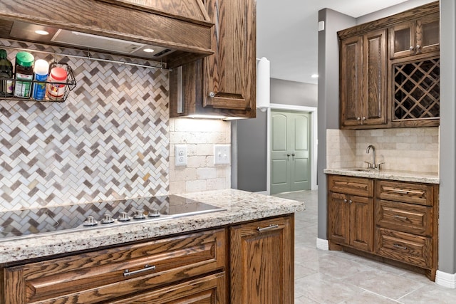 kitchen featuring light stone countertops, sink, backsplash, stovetop, and custom range hood