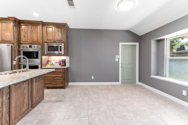 kitchen with decorative backsplash, light stone counters, stainless steel appliances, vaulted ceiling, and sink