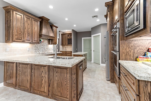 kitchen with kitchen peninsula, light stone countertops, custom range hood, stainless steel appliances, and sink