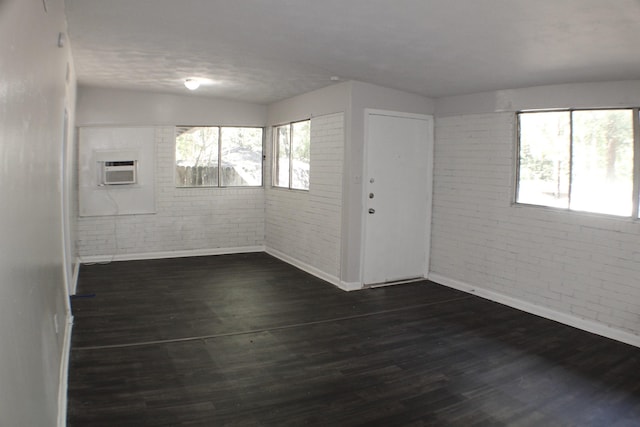 unfurnished room with dark hardwood / wood-style flooring, an AC wall unit, and brick wall