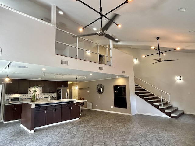 kitchen featuring a center island, tasteful backsplash, stainless steel fridge, a towering ceiling, and dark brown cabinets