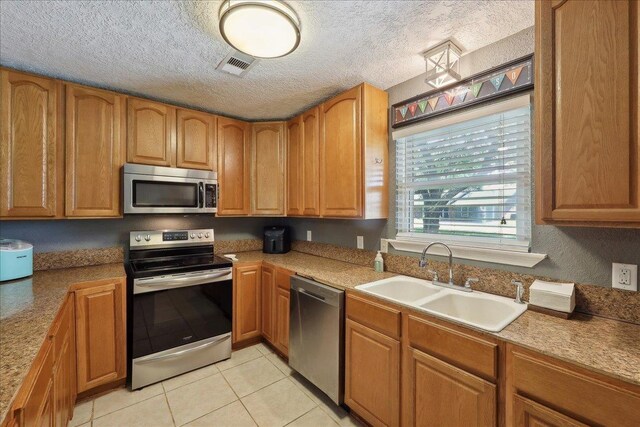 233 Spooner St, Orange, TX 77630 - kitchen with stainless steel appliances, a sink, light tile patterned floors, brown cabinets, and a textured ceiling