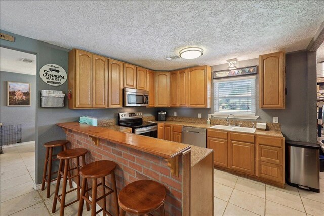 233 Spooner St, Orange, TX 77630 - kitchen with appliances with stainless steel finishes, a sink, light tile patterned floors, a kitchen bar, and a textured ceiling