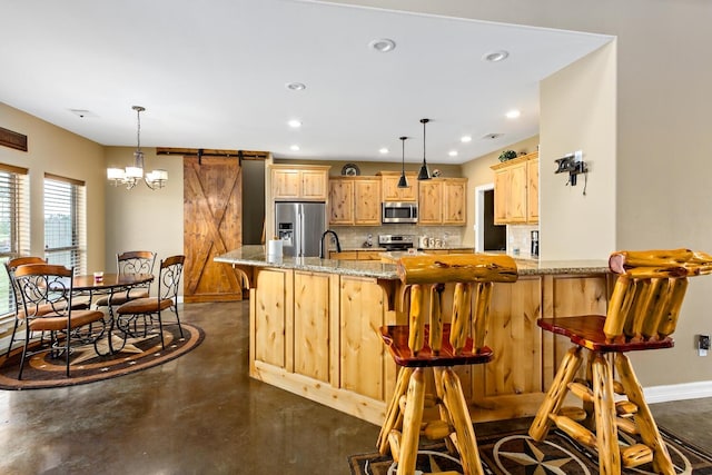 kitchen with light stone countertops, stainless steel appliances, a barn door, decorative light fixtures, and a kitchen bar