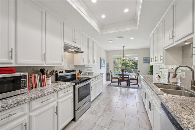 6650 Windwood Ln, Beaumont, TX 77706 - kitchen with appliances with stainless steel finishes, under cabinet range hood, a sink, a tray ceiling, and decorative backsplash