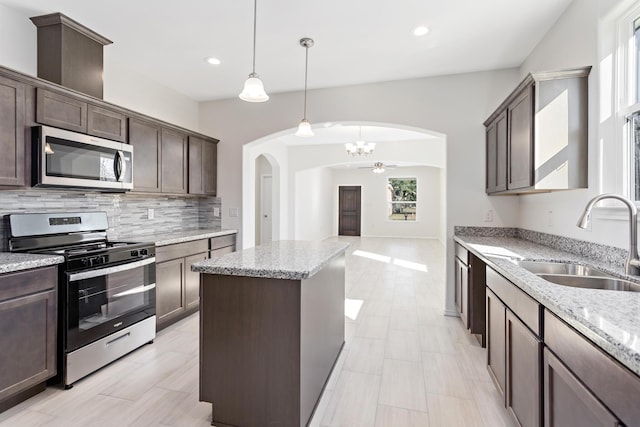 kitchen featuring appliances with stainless steel finishes, pendant lighting, light stone counters, sink, and backsplash