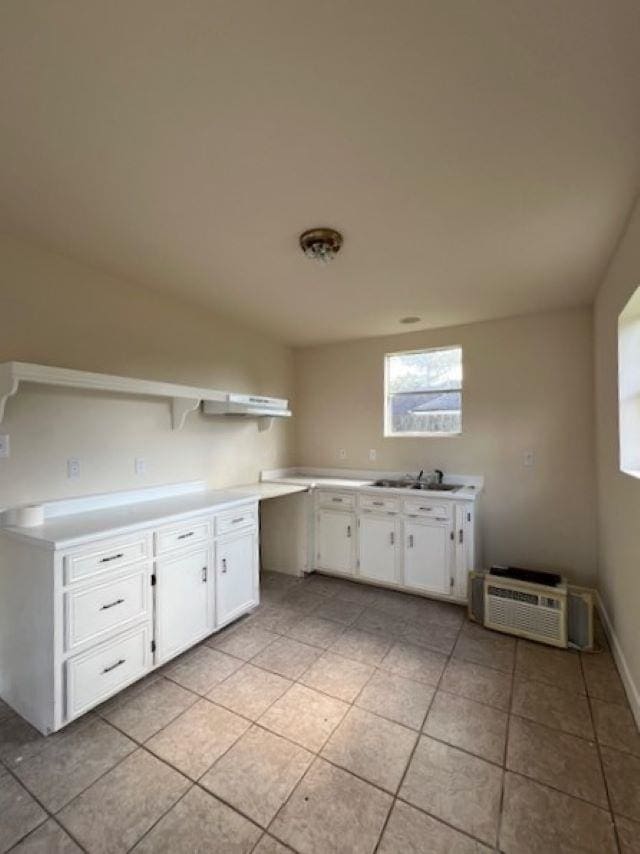 kitchen with white cabinetry, light tile patterned flooring, sink, and an AC wall unit