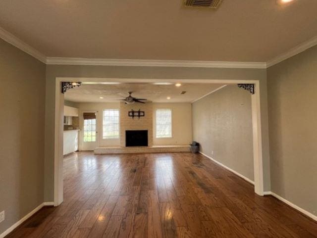 unfurnished living room with dark wood-type flooring, ornamental molding, a large fireplace, and ceiling fan