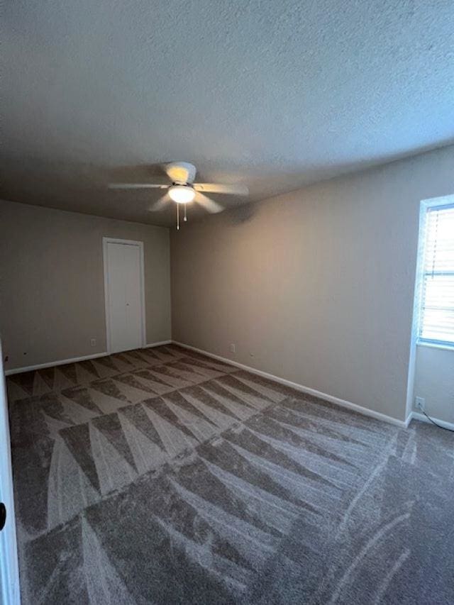 empty room with ceiling fan, a textured ceiling, and dark colored carpet