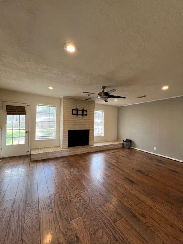 unfurnished living room featuring hardwood / wood-style flooring, ceiling fan, a fireplace, and a textured ceiling