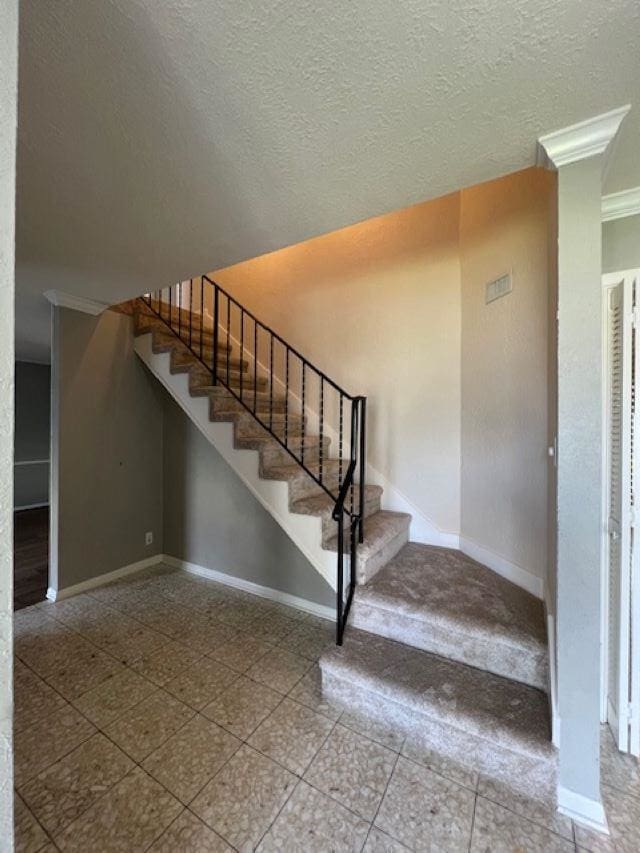 stairway with ornamental molding and a textured ceiling