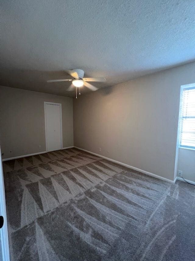 spare room featuring ceiling fan, dark carpet, and a textured ceiling