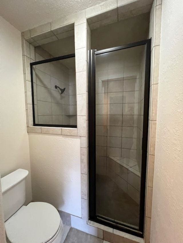 bathroom featuring toilet, an enclosed shower, and a textured ceiling