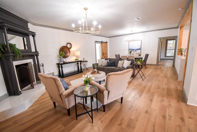 living room featuring a barn door, light hardwood / wood-style flooring, an inviting chandelier, and ornamental molding