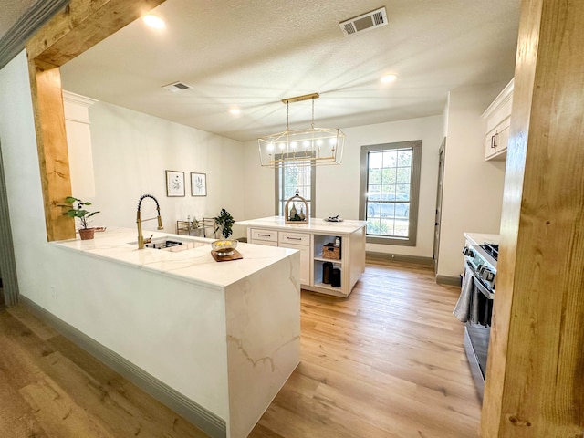 kitchen with pendant lighting, white cabinetry, an island with sink, and stainless steel stove