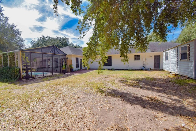 rear view of property with a lawn, glass enclosure, and a swimming pool