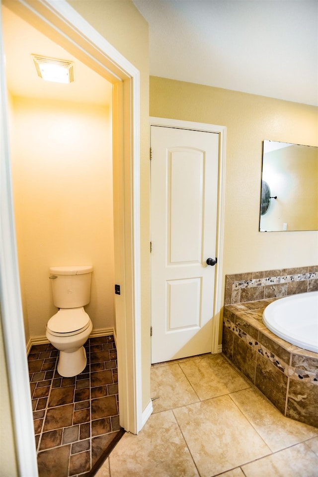 bathroom featuring tile patterned flooring, tiled bath, and toilet