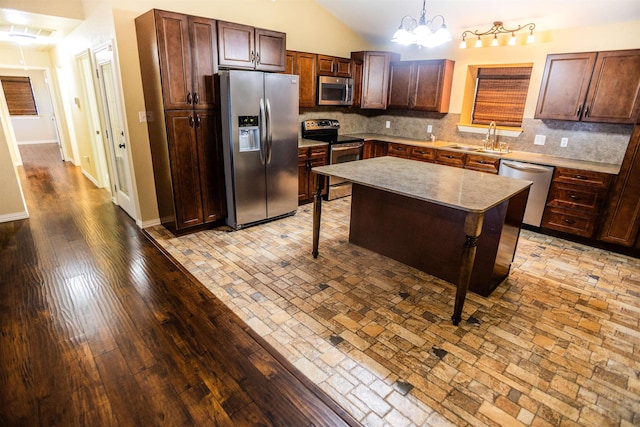 kitchen with sink, decorative light fixtures, appliances with stainless steel finishes, a kitchen island, and backsplash