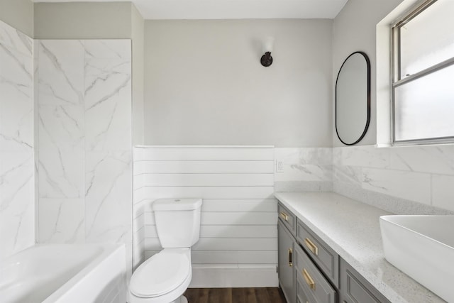 bathroom with wood finished floors, toilet, vanity, tile walls, and wainscoting