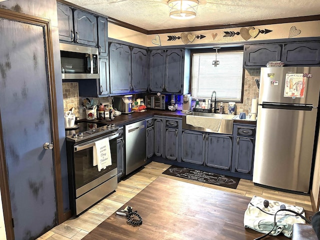 kitchen with appliances with stainless steel finishes, sink, light wood-type flooring, ornamental molding, and a textured ceiling