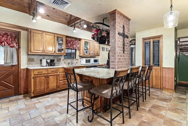134 Sherwood Trl, Silsbee, TX 77656 - kitchen featuring track lighting, white microwave, light stone finish floors, a sink, and wood walls